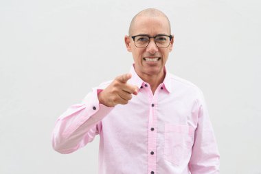 40 'lı yaşlarda, kel, olgun bir erkek. Sıradan pembe iş gömleği ve gözlük takıyor. Düz beyaz duvarın önünde duruyor. Şirket, iş ve yaşam tarzı kavramları için stüdyo tarzı görüntü kullanışlıdır.