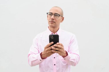 40 'lı yaşlarda, kel, olgun bir erkek. Sıradan pembe iş gömleği ve gözlük takıyor. Düz beyaz duvarın önünde duruyor. Şirket, iş ve yaşam tarzı kavramları için stüdyo tarzı görüntü kullanışlıdır.