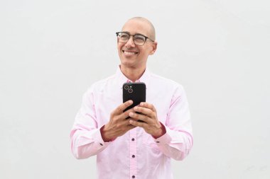 40 'lı yaşlarda, kel, olgun bir erkek. Sıradan pembe iş gömleği ve gözlük takıyor. Düz beyaz duvarın önünde duruyor. Şirket, iş ve yaşam tarzı kavramları için stüdyo tarzı görüntü kullanışlıdır.