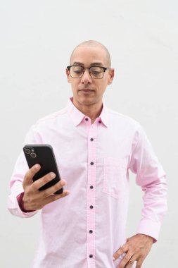 40 'lı yaşlarda, kel, olgun bir erkek. Sıradan pembe iş gömleği ve gözlük takıyor. Düz beyaz duvarın önünde duruyor. Şirket, iş ve yaşam tarzı kavramları için stüdyo tarzı görüntü kullanışlıdır.