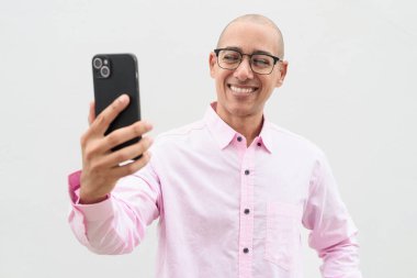 40 'lı yaşlarda, kel, olgun bir erkek. Sıradan pembe iş gömleği ve gözlük takıyor. Düz beyaz duvarın önünde duruyor. Şirket, iş ve yaşam tarzı kavramları için stüdyo tarzı görüntü kullanışlıdır.