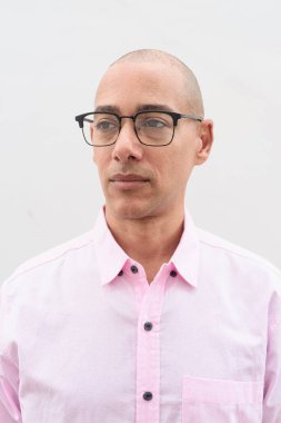 40 'lı yaşlarda, kel, olgun bir erkek. Sıradan pembe iş gömleği ve gözlük takıyor. Düz beyaz duvarın önünde duruyor. Şirket, iş ve yaşam tarzı kavramları için stüdyo tarzı görüntü kullanışlıdır.
