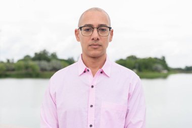 40 'lı yaşlarda, kel, olgun, pembe iş gömleği ve gözlük takan bir erkek doğa parkında gölün kenarında duruyor. Rahatlama, açık hava yaşam tarzı, rahatlık ve refah kavramı..