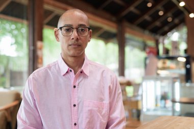 40 'lı yaşlarda kel, yetişkin bir erkek modern kahve dükkanında pembe günlük iş gömleği ve gözlük takıyor şehir yaşam tarzı, eğlence, kafe kültürü ve sosyal rahatlama kavramı..