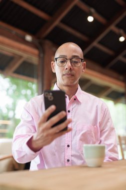 40 'lı yaşlarda kel, yetişkin bir erkek modern kahve dükkanında pembe günlük iş gömleği ve gözlük takıyor şehir yaşam tarzı, eğlence, kafe kültürü ve sosyal rahatlama kavramı..