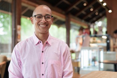 40 'lı yaşlarda kel, yetişkin bir erkek modern kahve dükkanında pembe günlük iş gömleği ve gözlük takıyor şehir yaşam tarzı, eğlence, kafe kültürü ve sosyal rahatlama kavramı..