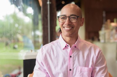 40 'lı yaşlarda kel, yetişkin bir erkek modern kahve dükkanında pembe günlük iş gömleği ve gözlük takıyor şehir yaşam tarzı, eğlence, kafe kültürü ve sosyal rahatlama kavramı..