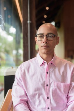 40 'lı yaşlarda kel, yetişkin bir erkek modern kahve dükkanında pembe günlük iş gömleği ve gözlük takıyor şehir yaşam tarzı, eğlence, kafe kültürü ve sosyal rahatlama kavramı..