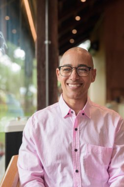 40 'lı yaşlarda kel, yetişkin bir erkek modern kahve dükkanında pembe günlük iş gömleği ve gözlük takıyor şehir yaşam tarzı, eğlence, kafe kültürü ve sosyal rahatlama kavramı..