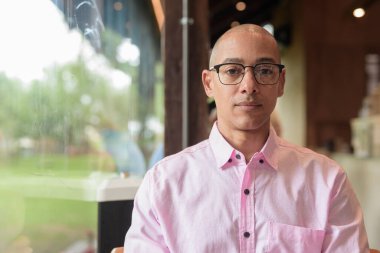 40 'lı yaşlarda kel, yetişkin bir erkek modern kahve dükkanında pembe günlük iş gömleği ve gözlük takıyor şehir yaşam tarzı, eğlence, kafe kültürü ve sosyal rahatlama kavramı..