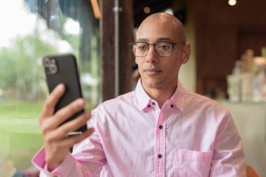 40 'lı yaşlarda kel, yetişkin bir erkek modern kahve dükkanında pembe günlük iş gömleği ve gözlük takıyor şehir yaşam tarzı, eğlence, kafe kültürü ve sosyal rahatlama kavramı..