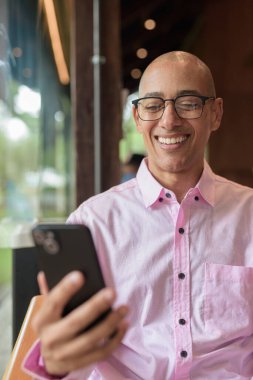 40 'lı yaşlarda kel, yetişkin bir erkek modern kahve dükkanında pembe günlük iş gömleği ve gözlük takıyor şehir yaşam tarzı, eğlence, kafe kültürü ve sosyal rahatlama kavramı..