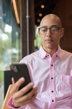 40 'lı yaşlarda kel, yetişkin bir erkek modern kahve dükkanında pembe günlük iş gömleği ve gözlük takıyor şehir yaşam tarzı, eğlence, kafe kültürü ve sosyal rahatlama kavramı..