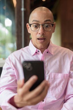 40 'lı yaşlarda kel, yetişkin bir erkek modern kahve dükkanında pembe günlük iş gömleği ve gözlük takıyor şehir yaşam tarzı, eğlence, kafe kültürü ve sosyal rahatlama kavramı..