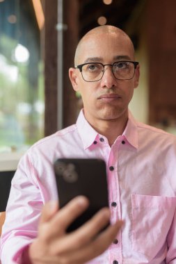 40 'lı yaşlarda kel, yetişkin bir erkek modern kahve dükkanında pembe günlük iş gömleği ve gözlük takıyor şehir yaşam tarzı, eğlence, kafe kültürü ve sosyal rahatlama kavramı..