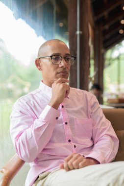 40 'lı yaşlarda kel, yetişkin bir erkek modern kahve dükkanında pembe günlük iş gömleği ve gözlük takıyor şehir yaşam tarzı, eğlence, kafe kültürü ve sosyal rahatlama kavramı..