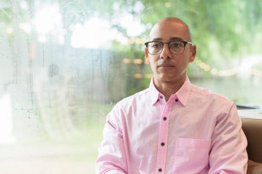 40 'lı yaşlarda kel, yetişkin bir erkek modern kahve dükkanında pembe günlük iş gömleği ve gözlük takıyor şehir yaşam tarzı, eğlence, kafe kültürü ve sosyal rahatlama kavramı..