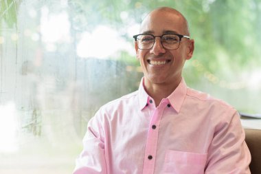 40 'lı yaşlarda kel, yetişkin bir erkek modern kahve dükkanında pembe günlük iş gömleği ve gözlük takıyor şehir yaşam tarzı, eğlence, kafe kültürü ve sosyal rahatlama kavramı..