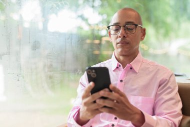 40 'lı yaşlarda kel, yetişkin bir erkek modern kahve dükkanında pembe günlük iş gömleği ve gözlük takıyor şehir yaşam tarzı, eğlence, kafe kültürü ve sosyal rahatlama kavramı..