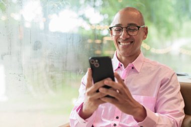 40 'lı yaşlarda kel, yetişkin bir erkek modern kahve dükkanında pembe günlük iş gömleği ve gözlük takıyor şehir yaşam tarzı, eğlence, kafe kültürü ve sosyal rahatlama kavramı..