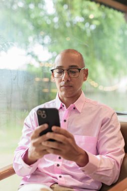 40 'lı yaşlarda kel, yetişkin bir erkek modern kahve dükkanında pembe günlük iş gömleği ve gözlük takıyor şehir yaşam tarzı, eğlence, kafe kültürü ve sosyal rahatlama kavramı..