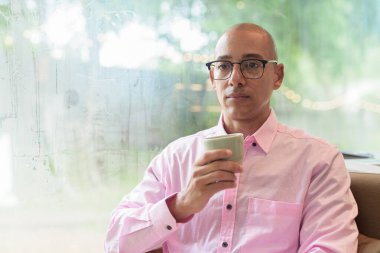 40 'lı yaşlarda kel, yetişkin bir erkek modern kahve dükkanında pembe günlük iş gömleği ve gözlük takıyor şehir yaşam tarzı, eğlence, kafe kültürü ve sosyal rahatlama kavramı..