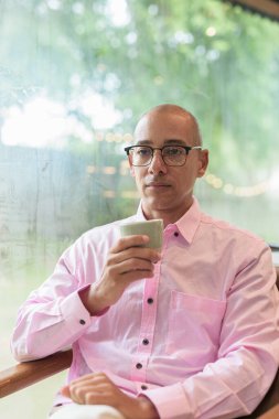 40 'lı yaşlarda kel, yetişkin bir erkek modern kahve dükkanında pembe günlük iş gömleği ve gözlük takıyor şehir yaşam tarzı, eğlence, kafe kültürü ve sosyal rahatlama kavramı..