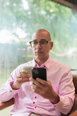 40 'lı yaşlarda kel, yetişkin bir erkek modern kahve dükkanında pembe günlük iş gömleği ve gözlük takıyor şehir yaşam tarzı, eğlence, kafe kültürü ve sosyal rahatlama kavramı..