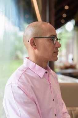 40 'lı yaşlarda kel, yetişkin bir erkek modern kahve dükkanında pembe günlük iş gömleği ve gözlük takıyor şehir yaşam tarzı, eğlence, kafe kültürü ve sosyal rahatlama kavramı..