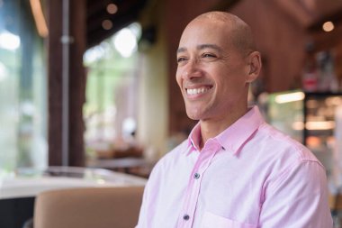 40 'lı yaşlarda kel, yetişkin bir erkek modern kahve dükkanında pembe günlük iş gömleği ve gözlük takıyor şehir yaşam tarzı, eğlence, kafe kültürü ve sosyal rahatlama kavramı..