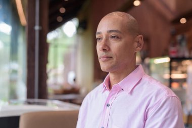 40 'lı yaşlarda kel, yetişkin bir erkek modern kahve dükkanında pembe günlük iş gömleği ve gözlük takıyor şehir yaşam tarzı, eğlence, kafe kültürü ve sosyal rahatlama kavramı..