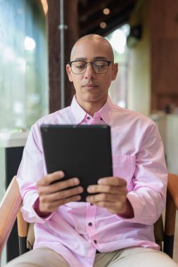 40 'lı yaşlarda kel, yetişkin bir erkek modern kahve dükkanında pembe günlük iş gömleği ve gözlük takıyor şehir yaşam tarzı, eğlence, kafe kültürü ve sosyal rahatlama kavramı..