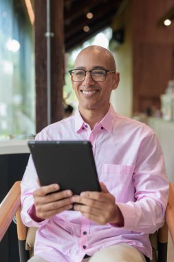 40 'lı yaşlarda kel, yetişkin bir erkek modern kahve dükkanında pembe günlük iş gömleği ve gözlük takıyor şehir yaşam tarzı, eğlence, kafe kültürü ve sosyal rahatlama kavramı..