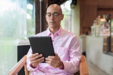 40 'lı yaşlarda kel, yetişkin bir erkek modern kahve dükkanında pembe günlük iş gömleği ve gözlük takıyor şehir yaşam tarzı, eğlence, kafe kültürü ve sosyal rahatlama kavramı..