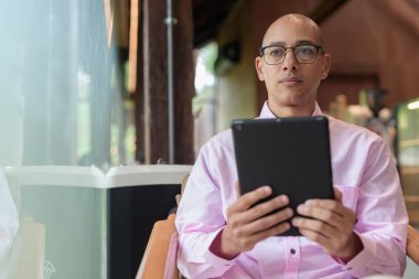 40 'lı yaşlarda kel, yetişkin bir erkek modern kahve dükkanında pembe günlük iş gömleği ve gözlük takıyor şehir yaşam tarzı, eğlence, kafe kültürü ve sosyal rahatlama kavramı..