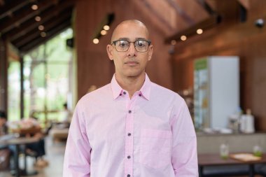 40 'lı yaşlarda kel, yetişkin bir erkek modern kahve dükkanında pembe günlük iş gömleği ve gözlük takıyor şehir yaşam tarzı, eğlence, kafe kültürü ve sosyal rahatlama kavramı..