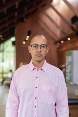 40 'lı yaşlarda kel, yetişkin bir erkek modern kahve dükkanında pembe günlük iş gömleği ve gözlük takıyor şehir yaşam tarzı, eğlence, kafe kültürü ve sosyal rahatlama kavramı..