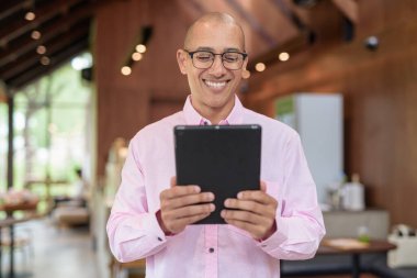 40 'lı yaşlarda kel, yetişkin bir erkek modern kahve dükkanında pembe günlük iş gömleği ve gözlük takıyor şehir yaşam tarzı, eğlence, kafe kültürü ve sosyal rahatlama kavramı..