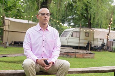 40 'lı yaşlarda kel, olgun bir erkek pembe gömlek ve gözlük takıyor. Kamp alanı çevresi ve karavan geçmişi var. Açık hava eğlence ortamında seyahat, turizm ve yaşam tarzı kavramı.