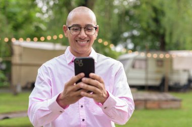 40 'lı yaşlarda kel, olgun bir erkek pembe gömlek ve gözlük takıyor. Kamp alanı çevresi ve karavan geçmişi var. Açık hava eğlence ortamında seyahat, turizm ve yaşam tarzı kavramı.