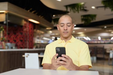 Yetişkin, kel bir İtalyan 'ın portresi modern bir lokantada oturmuş uzaktan kumandayla telefon kullanıyor.