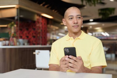 Yetişkin, kel bir İtalyan 'ın portresi modern bir lokantada oturmuş uzaktan kumandayla telefon kullanıyor.