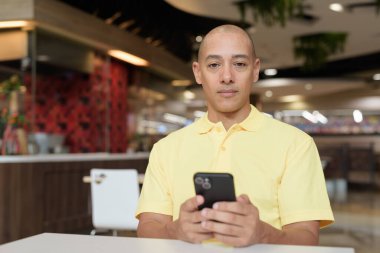 Yetişkin, kel bir İtalyan 'ın portresi modern bir lokantada oturmuş uzaktan kumandayla telefon kullanıyor.