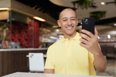 Yetişkin, kel bir İtalyan 'ın portresi modern bir lokantada oturmuş uzaktan kumandayla telefon kullanıyor.