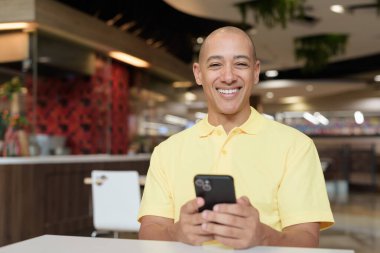 Yetişkin, kel bir İtalyan 'ın portresi modern bir lokantada oturmuş uzaktan kumandayla telefon kullanıyor.