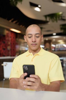 Yetişkin, kel bir İtalyan 'ın portresi modern bir lokantada oturmuş uzaktan kumandayla telefon kullanıyor.