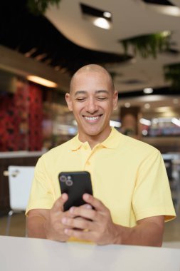 Yetişkin, kel bir İtalyan 'ın portresi modern bir lokantada oturmuş uzaktan kumandayla telefon kullanıyor.