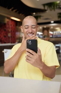 Yetişkin, kel bir İtalyan 'ın portresi modern bir lokantada oturmuş uzaktan kumandayla telefon kullanıyor.