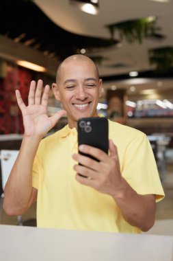 Yetişkin, kel bir İtalyan 'ın portresi modern bir lokantada oturmuş uzaktan kumandayla telefon kullanıyor.