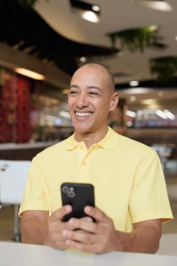 Yetişkin, kel bir İtalyan 'ın portresi modern bir lokantada oturmuş uzaktan kumandayla telefon kullanıyor.